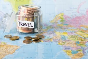 Travel budget concept. Money saved for vacation in glass jar on map background