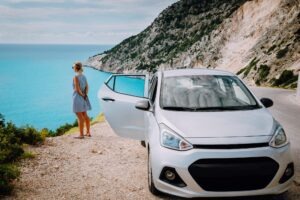 Women near rented car with open door enjoying Myrtos Beach. Travel vocation concept. Kefalonia