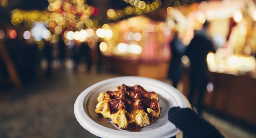 Hand in winter glove holding waffle with melted chocolate. Christmas market in Tallinn, Estonia.