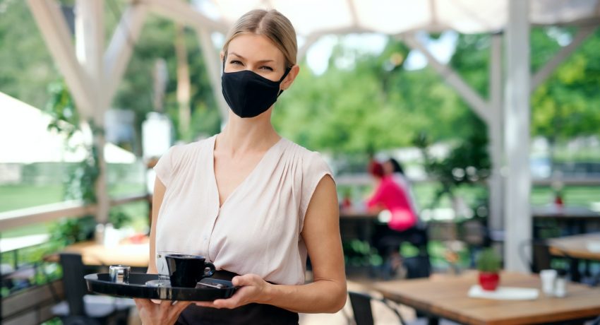 Waitress with face mask serving customers outdoors on terrace restaurant