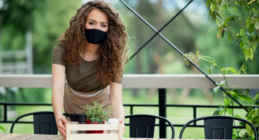 Waitress with face mask working outdoors on terrace restaurant